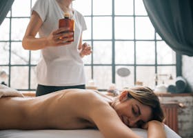 A woman enjoying a relaxing massage in a serene spa environment, holding a bottle of essential oil.