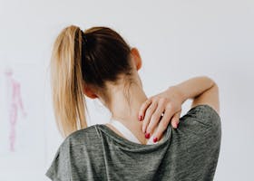 A woman in casual clothing holds her neck, indicating pain or discomfort.